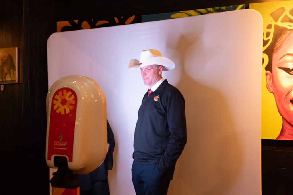 Man wearing a cowboy hat posing in front of a photo booth backdrop at an event, showcasing a unique photo experience.